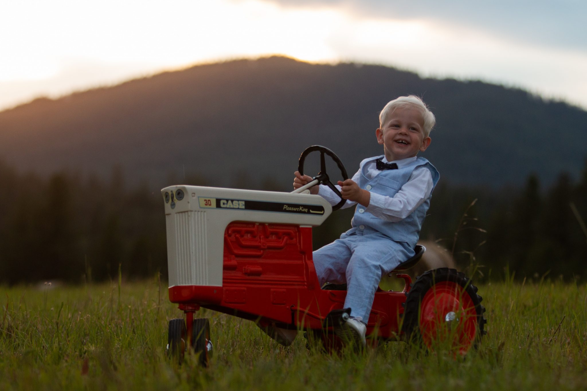 boy in blue jacket riding red and white tractor on green grass field during daytime