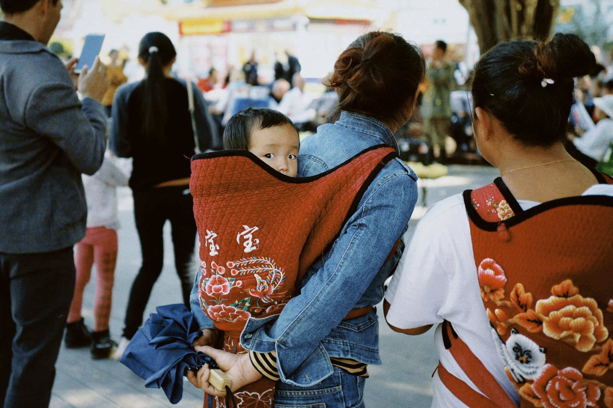 woman in blue denim jacket carrying baby in orange and white shirt