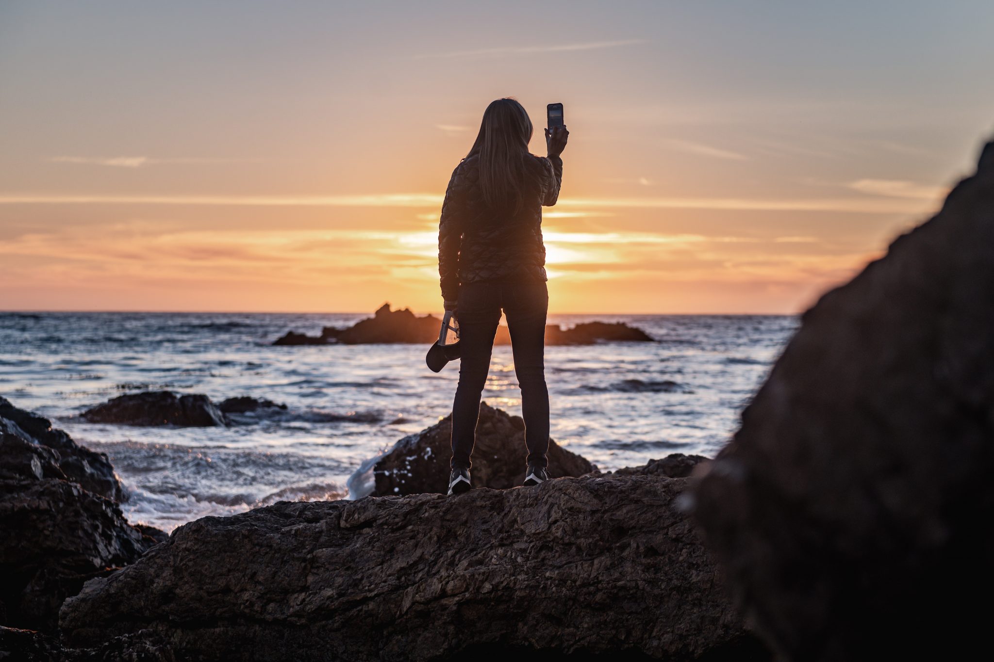 silhouette of woman standing on rock formation near body of water during sunset