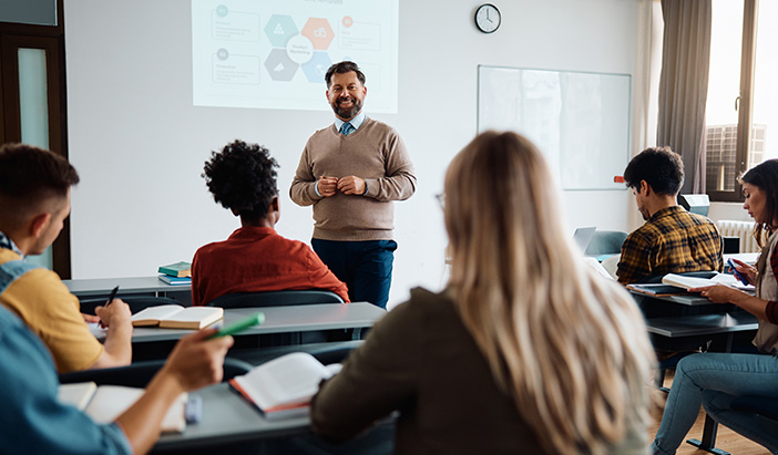 Happy mature teacher talks to his students while holding presentation in lecture hall. Teacher talking to students